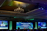 Photo taken by myself. It is an image of the conference screen at Disability:IN 2023 Confernece that says “luncheon planetary, disabled and proud. Celebrating our disability experience.” The screen shows up as a blue background with white text and green and blue stripes across it the room is rather dark lit by different lights on the ceiling.