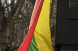 A flags hangs from a balcony. Its colors are yellow, green, & red.
