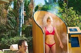 A woman in a red bikini having sunscreen applied within the SnappyScreen spraybooth