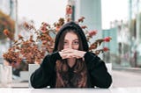 Young woman in black hoodie looking straight with a plant behind her