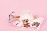 Broken piggy bank — pink background — hammer