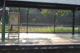 A nobody platform of a railway station in the late afternoon of warm sunlight, with backlight shades of green and see-through fence as backdrop.