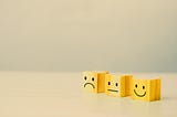 Three wooden blocks with emotion faces of sad, neutral and happy on them
