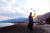 Woman standing by a lake smiling and juggling balls.