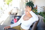 Black person with green locs seated outside on chair, possibly wondering why white people are still trying to do this hair this way and get away with it.