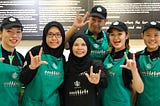 A group of Starbucks staffs from the Starbucks Signing Store in Penang posing for a group photo. The team are wearing the Starbucks Signing apron and hand gesturing ”rock on”.