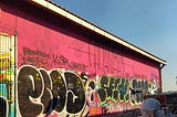 Street art graffiti along a pink-sided warehouse wall