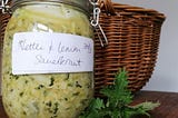 A jar of nettle and lemon sauerkraut next to a wicker basket with nettles