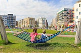 Two children sitting on a hammock looking at clean cities with mid-rise building and greeneries in front of them