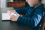 A child sitting at table using a tablet