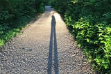 Elongated shadow of self on gravel path