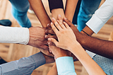 Office of a variety of skin colors stacking their hands to do a team cheer.