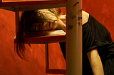 Woman in black rests on arm, exhausted. Red background.