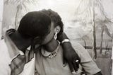 A Black couple kissing in front of a beach themed back drop