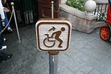 An erroneous wheelchair sign in disneyland depicts the user getting up out of it to get ready for a ride.