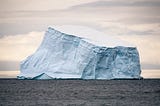 An iceberg in the middle of the ocean with clouds behind