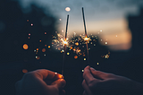 Two hands are holding lit-up sparklers