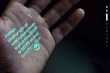 The image shows a human hand with text and graphics projected onto its palm, resembling an augmented user interface from a promotional video for a product called »Humane AI Pin«. The projection includes text with pricing information for »Vintage Photographs« and an icon, suggesting an interactive advertisement or shopping application.