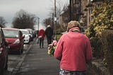 elderly woman carrying a bouquet of flowers while walking down the street