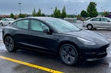 Black tesla model 3 car with white seats in a parking lot on a rainy day