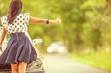 A young woman in a short skirt hitchhiking for a ride.