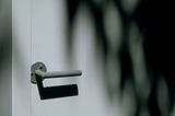 Gray door handle casting a shadow on a light colored door.