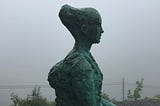 Grey statue of a woman with fog in the background.