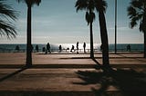 Picture of a beautiful beach day with shadows of people walking on a boardwalk and palm trees
