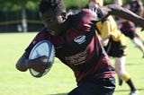 a young man runs with a rugby ball under his arm.