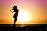 Stock image of a woman’s silhouette in front of a beautiful sunset. She is carefree and happy because less is more.