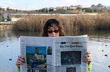 A young woman wearing sunglasses and a frown on her face reads the newspaper.