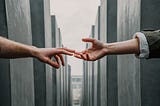 Two hands reaching out to touch with a backdrop of the Jewish Holocaust memorial in Berlin.