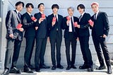 BTS lined up together in dark suits holding red diplomatic passports