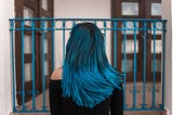 girl standing in front of gate with back turned showing teal blue hair