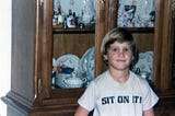 Author around age 9 wearing a shirt with iron on letters that say, “Sit on it!”