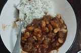 A bowl containing white rice, beef chili that appears to have been made with cannelini beans.