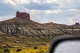 A colorful tall brown plateau above striated layers of sediment in a mountainside, yellow bed of flower bloom below