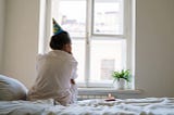 woman sits with back to the camera, wearing a party hat, cupcake with candle next to her