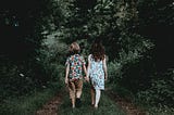 Two children walking down a forest path while holding hands