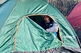 A man looks out through an unzipped tent on the sidewalk.