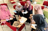 Five women sitting in desks in a circle, doing an activity with strips of paper. They are taking part in World Learning’s English Learning Teacher Training program.