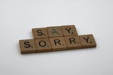 Scrabble tiles that spell out the words “Say Sorry”