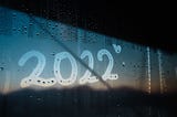 Alt text: On the tempered glass of a misty car window, someone has finger-painted the year “2022.” They’ve drawn a little heart after the final “2,” and through the window, you can see a sunset. This, I think, is what we are all doing: sending each other hearts through the glass.