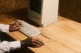 An old computer with one hand on the keyboard and one on the mouse