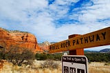 Sign: Bell Rock Pathway with red rock, brush, clouds sparsed with blue sky