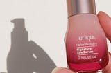 A woman’s hand holds a red bottle of Jurlique eye serum, with a shadow cast behind