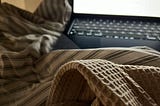 An open laptop on a messy bed from the perspective of someone using the laptop in bed.