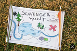 A scenic map, sitting on the grass or straw, that says Scavenger Hunt in big black letter at the top, and has a big red X.