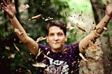 Young man in a purple t-shirt throws dried leaves into the air.