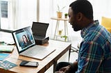 A man on a video call with a woman, smiling at his laptop